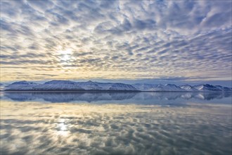 Snow covered mountains at Billefjorden at sunset and clouds reflected in the Arctic sea