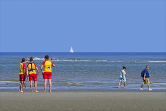 Three young Belgian lifeguards watching over empty sea along the North Sea coast in summer at Koksijde
