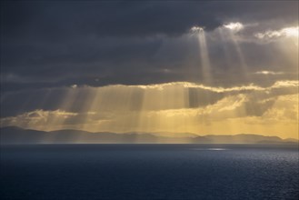Sunrays bursting through dense sheet of rain clouds over sea water at sunset