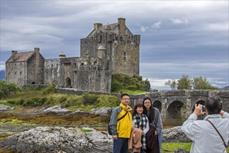 Asian tourists posing in front of Eilean Donan Castle in Loch Duich