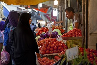 Iranian Muslim women wearing scarves buying vegetables and red tomatoes at food market booth in Gorgan