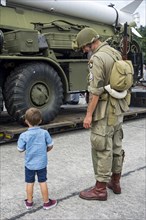Little boy and WW2 reenactor in US soldier outfit looking at missile truck at World War Two militaria fair