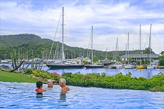 Sailing boats and yachts moored in English Harbour and Western tourists in swimming pool on the island Antigua