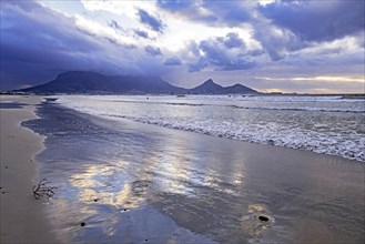 Rain clouds over the Table Mountain and sandy Sunset Beach on Woodbridge Island near Cape Town