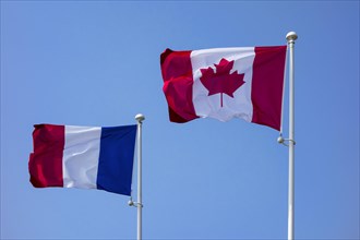 National Canadian and French flags on flagpoles flying in the wind against blue sky