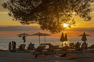 Tourists on the beach in reclining chairs enjoying sunset over the Adriatic Sea at Ankaran along the Slovenian Riviera