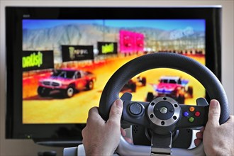 Steering wheel controller in front of television screen showing cars in racing game