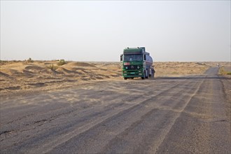 Truck crossing the Karakum desert in Turkmenistan and wind blowing sand from the dunes over the road