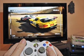 Hands holding controller in front of television screen showing cars in racing game