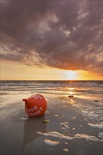 Seascape showing orange buoy on the beach at low tide and sunset over the Wadden Sea