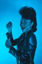 A closeup portrait of a funky stylish woman in a leather jacket posing illuminated by blue neon lights