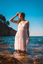 A young caucasian brunette in a white dress bathing in the sea water
