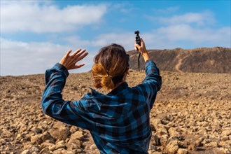 A young woman taking photos with a handheld camera next to the Crater of the Calderon Hondo volcano near Corralejo