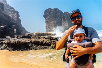 A young father with his baby in the Roque del Moro of the Cofete beach of the natural park of Jandia