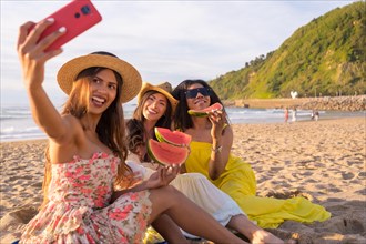Friends eating watermelon and taking a selfie on the beach during sunset