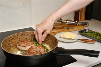 Hand of man add thyme into hot frying pan with beef steak