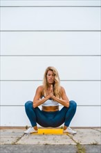 Yoga with blonde caucasian girl doing exercise on a yellow mat with white wall in the background