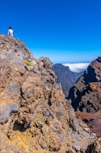 A young woman sits resting and looking at the views of the Roque de los Muchachos national park on top of the Caldera de Taburiente
