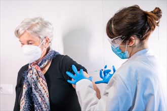An elderly woman receiving the injection of the coronavirus vaccine by a doctor to receive the antibodies