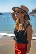 Blonde woman spending the holidays in a luxury hotel on a terrace wearing a hat with sunglasses