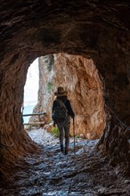 A young hiker in the tunnel of the trail in the Penon de Ifach Natural Park with the city of Calpe in the background