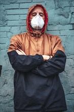 A young man in mask and hood leaning against a wall staring intently. First walks of the uncontrolled Covid-19 pandemic
