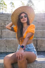 Lifestyle of a young caucasian brunette walking in the summer in a park in the city. Portrait of the girl with a hat at sunset