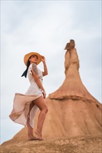 Brunette Caucasian model with a white dress and a straw hat in the Castildetierra of the Bardenas Reales desert