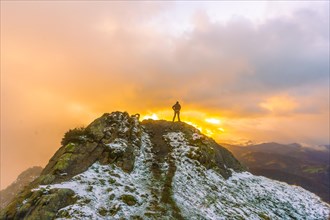 A young man on top of the mountain in the snowy winter orange sunset