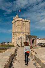 A young woman on vacation next to Saint Nicolas Tower of La Rochelle. Coastal town in southwestern France