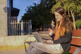 Woman waving at the laptop sitting on a bench during a video call online