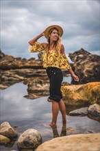 Caucasian blonde girl in a floral shirt and black shorts in a natural landscape by the sea at sunset
