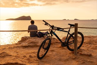 A tourist cycling on Cala Comte beach on the island of Ibiza. Sunset. Balearic
