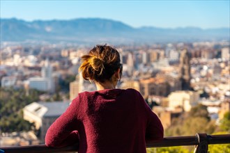 A young woman looking at the views of the city and the Cathedral of the Incarnation of Malaga from the Castillo de Gibralfaro in the city of Malaga