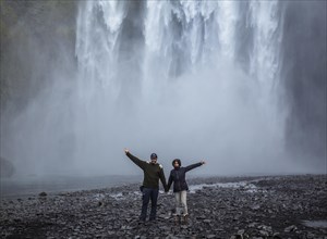 A couple with open arms at the bottom of the Skogafoss waterfall in the golden circle of the south of Iceland