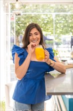 Woman drinking a healthy orange organic juice standing on a counter of a cafeteria