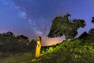 Brunette girl in yellow dress looking at the beautiful milky way on Mount Erlaitz in the town of Irun