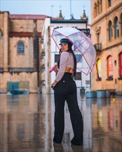 Posing of a young brunette Latina with a leather cap in the autumn rain with a transparent umbrella in the city