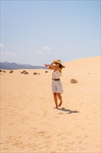 A young tourist wearing a hat walking through the dunes of the Corralejo Natural Park