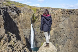 A young woman looking at the waterfall above Hengifoss from above. Iceland