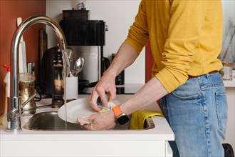 Unrecognizable man washing dishes in the kitchen with sponge