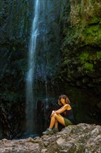 A young woman at the waterfall at the end of the waterfall trail at Levada do Caldeirao Verde