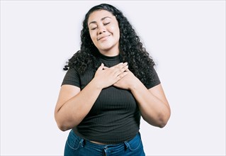 Positive latin girl with hands on chest. Grateful young woman with hands on chest. Grateful teenage girl smiling with hands on chest isolated