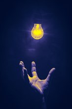 Hand reaches from below for luminous light bulb