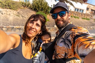 A father with his son in his backpack and the mother on vacation on the beach of Ajuy