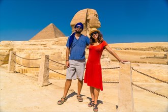 A tourist couple at The Great Sphinx of Giza and in the background the Pyramids of Giza
