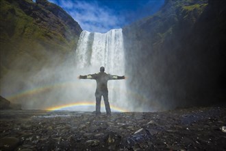 A tourist with open arms at the bottom of the Skogafoss waterfall in the golden circle