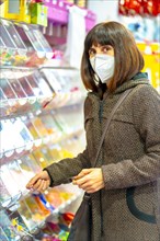 A caucasian brunette with a mask buying jelly beans in a pastry shop. First walks of the uncontrolled Covid-19 pandemic