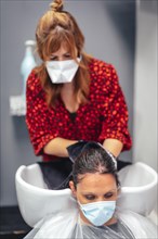 Hairdresser with mask and gloves washing the client's hair with soap and water. Reopening with security measures for hairdressers in the Covid-19 pandemic