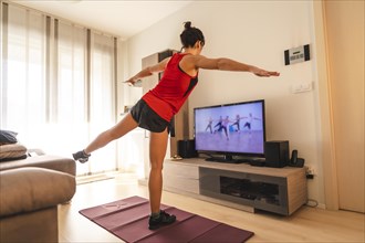 A young woman doing stretching in the room following the instructions of the online teacher. Sport in the covid19 quarantine at home